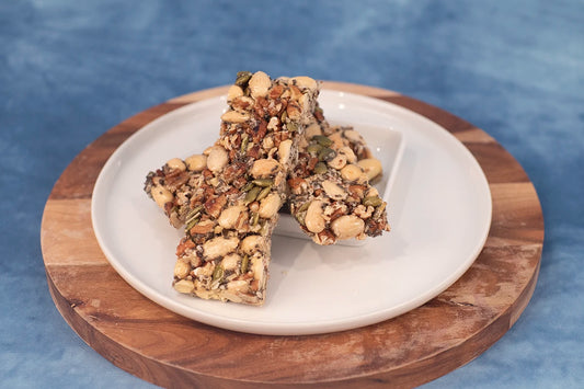 Keto nut bars on a wooden platter with slivered almonds, pecans, pumpkin seeds, and shredded coconut.