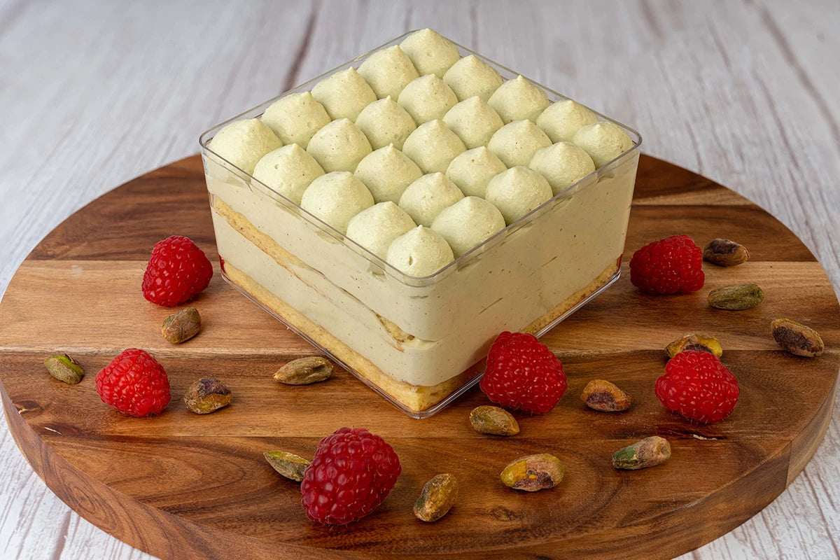 Pistachio raspberry box cake dessert on a wooden table with raspberries and pistachios