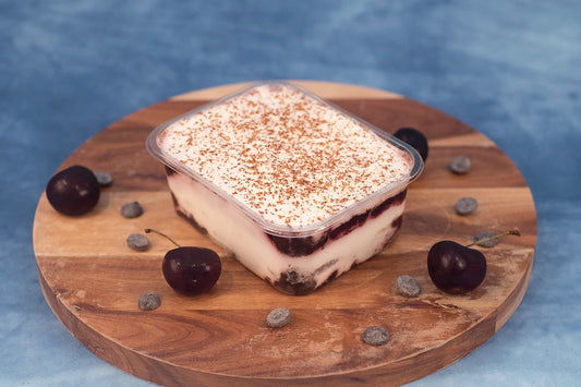 Keto black forest box cake dessert on a wooden platter with organic cherries and chocolate.