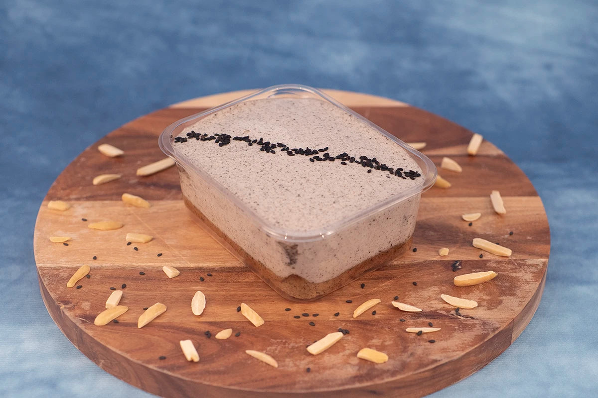 Keto black sesame box cake dessert on a wooden platter with black sesame and almonds.
